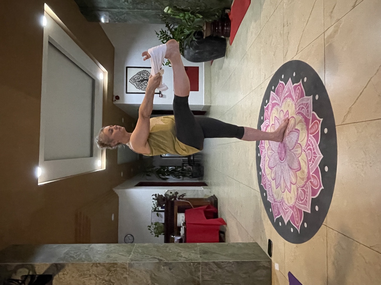 Standing hand-to-big-toe balance pose on a lotus mandala mat