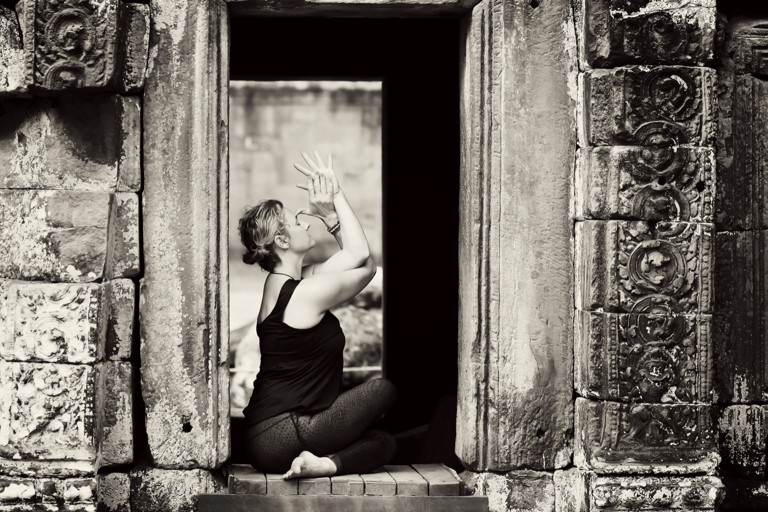 Heidi Van Maanenberg, founder of b.YOGA Practice, in eagle arms at a temple window in Angkor, Cambodia